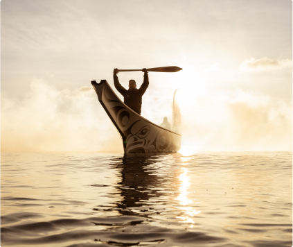 Man in a canoe at sunrise holding a paddle up over his head